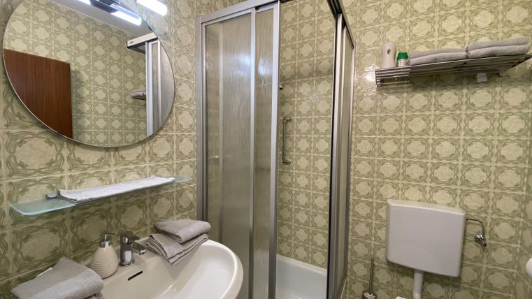 A small bathroom with a shower and a sink. The walls are adorned with decorative wallpaper and there is a round mirror.