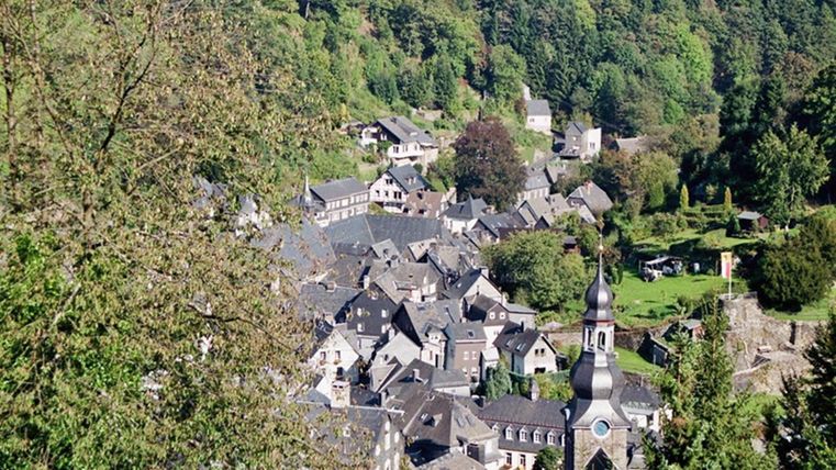 Een pittoresk dorpje te midden van groene bossen, met oude gebouwen en een kerk in het midden. De omgeving is gekenmerkt door natuur en heuvels.