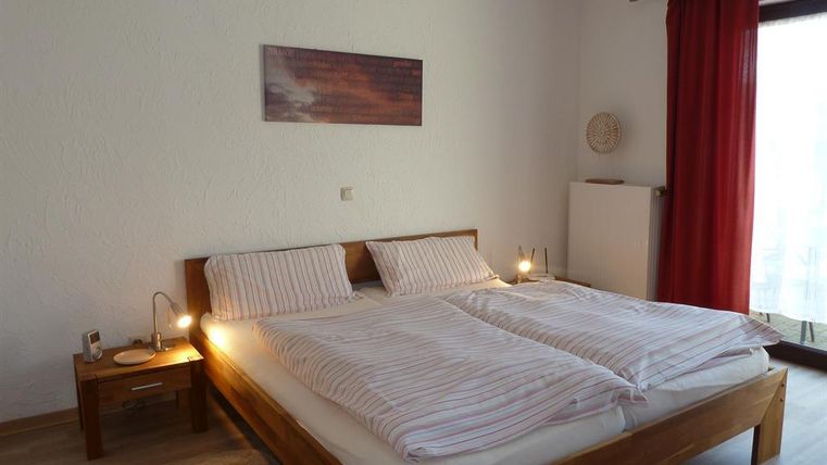 A cozy bedroom with a large double bed and striped bedspreads. The room has a warm tone and large windows with red curtains.