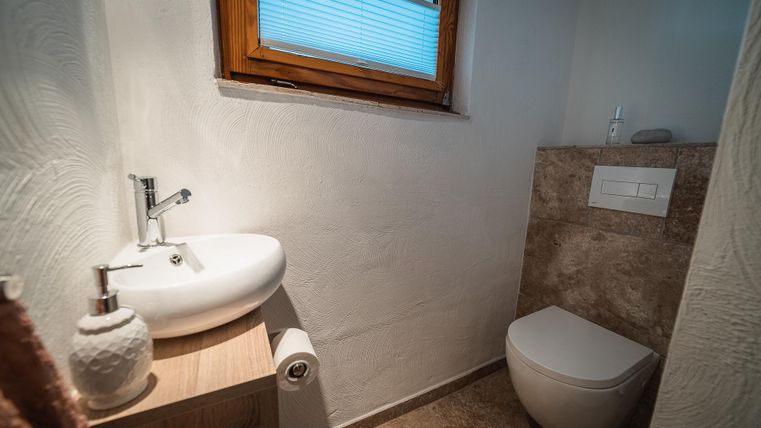 Een moderne badkamer met een witte wastafel en een toilet. Het raam laat natuurlijk licht binnenkomen en zorgt voor een heldere sfeer.