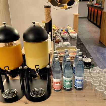 A selection of drinks, including juice and mineral water, is on a table. In the background, various snacks and glasses can be seen.
