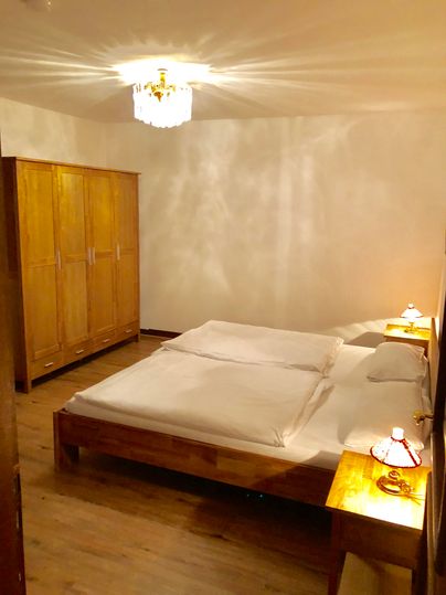 Ein einfaches Schlafzimmer mit einem großen Doppelbett und Holzschränken. An den Wänden reflektiert das Licht sanfte Schatten.
