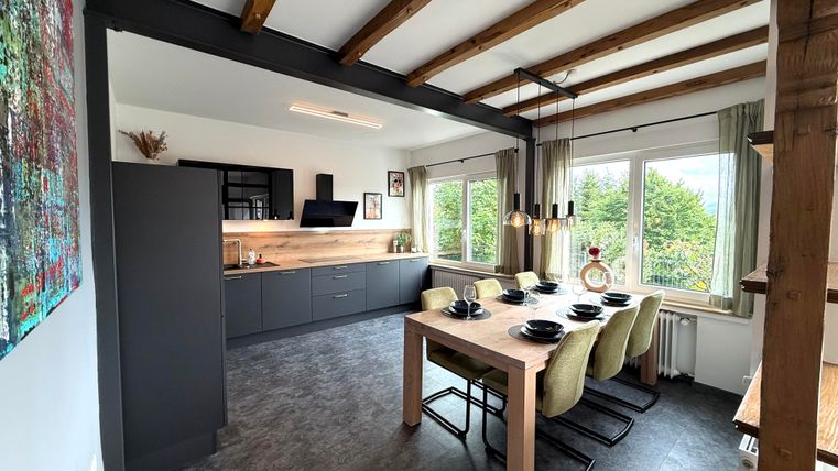 Een moderne keuken met een grote eettafel en comfortabele stoelen. Grote ramen bieden uitzicht op het groen.