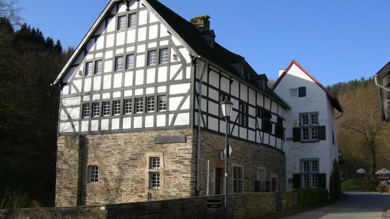 A historical timber-framed house with a stone base and a clear sky. The architecture exhibits traditional elements and harmonizes with the surroundings.