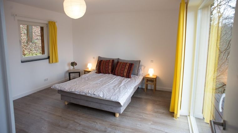 A bright bedroom with a large bed and colorful cushions. Yellow curtains and soft lighting create an inviting atmosphere.