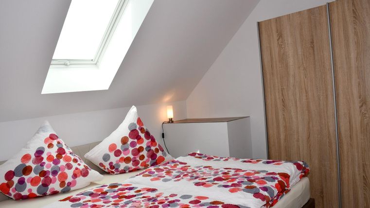 Een gezellige slaapkamer met een tweepersoonsbed en kleurige kussens. Er is een kledingkast en een dakraam dat daglicht binnenlaat.
