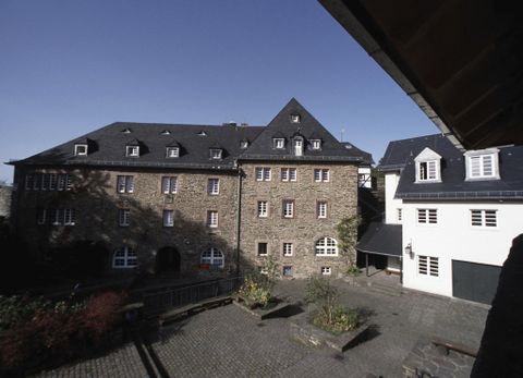 Ein historisches Gebäude aus Stein mit mehreren Fenstern. Der Innenhof ist ruhig mit einigen Pflanzen.