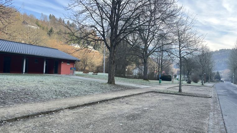 A quiet park with bare trees and frosty ground. In the background, buildings and gentle hills can be seen.