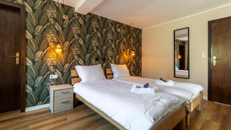A modern bedroom with two single beds and a green plant wall. The warm light sources create a cozy atmosphere.