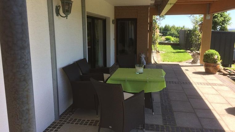 Eine gemütliche Terrasse mit einem Tisch und Stühlen. Der Bereich ist von einem gepflegten Garten umgeben.