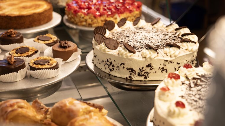 Eine Auswahl an Kuchen und süßen Leckereien, darunter Torten, Muffins und Gebäck. Die Auslage ist appetitlich und vielfältig.