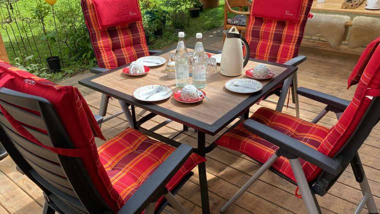 A beautifully set table on a terrace with red chairs. On the table are drinks and plates for a cozy gathering.