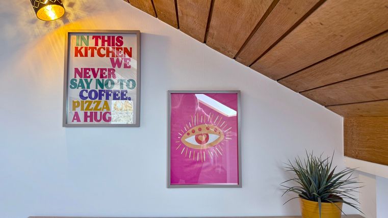 Een gezellige kamer met twee kleurrijke schilderijen aan de muur. Op de voorgrond staat een pot met een plant.