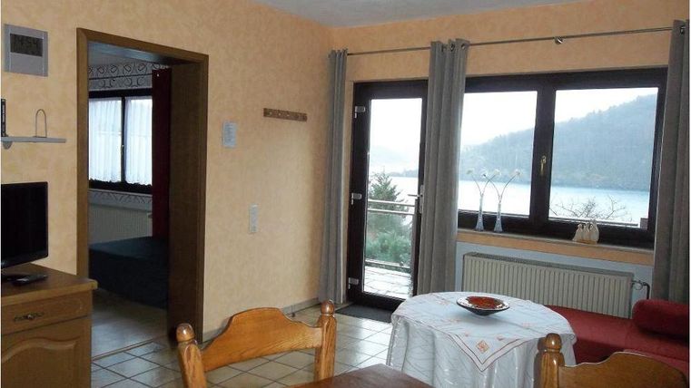 A cozy living space with a dining table and a view of the lake. Large windows allow plenty of light in and offer a view of the surrounding nature.