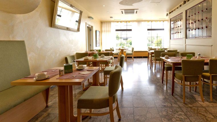 A modern restaurant with bright walls and elegant furniture. The tables are neatly set, and there is plenty of natural light.