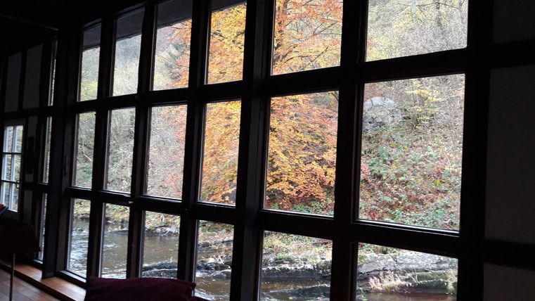 A view through large windows of a river and colorful autumn trees. The nature in the background harmonizes with the cozy interior.