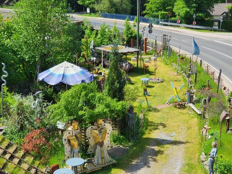 Een originele tuin met verschillende sculpturen en een grote parasol. De groene omgeving en het pad leiden naar een straat.