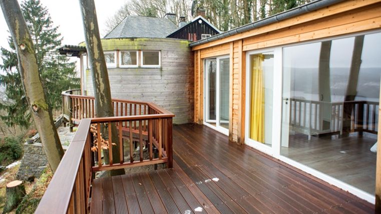 A modern wooden terrace surrounded by trees. The view of the landscape is clear and inviting.