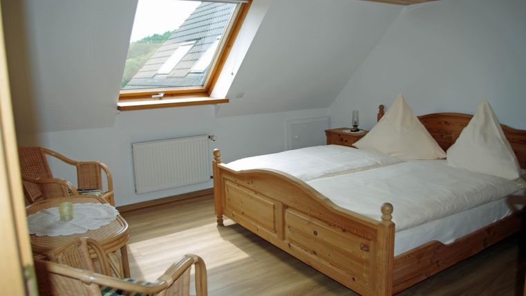A cozy bedroom with a double bed and two chairs. Large skylights provide plenty of daylight.