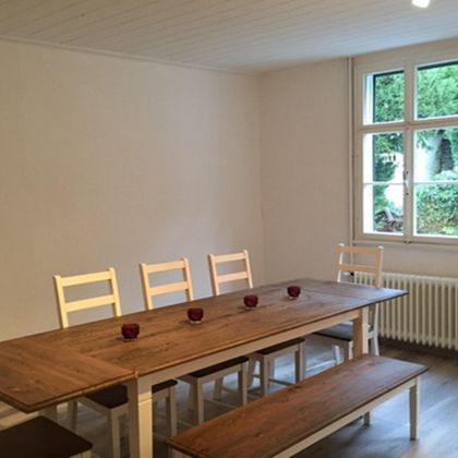 A bright dining room with a wooden tray and white chairs. A green view can be seen through the window.