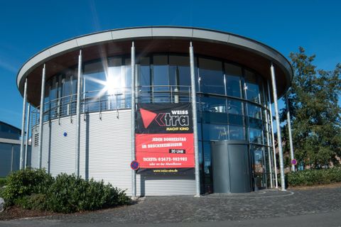 Een modern gebouw met grote ramen en een rond dak. Aan de gevel is een opvallend reclamebord te zien.