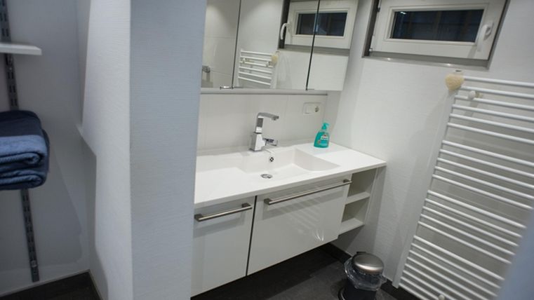 A modern bathroom with a clean sink and large mirrors. Towels are neatly stacked and a radiator is visible.