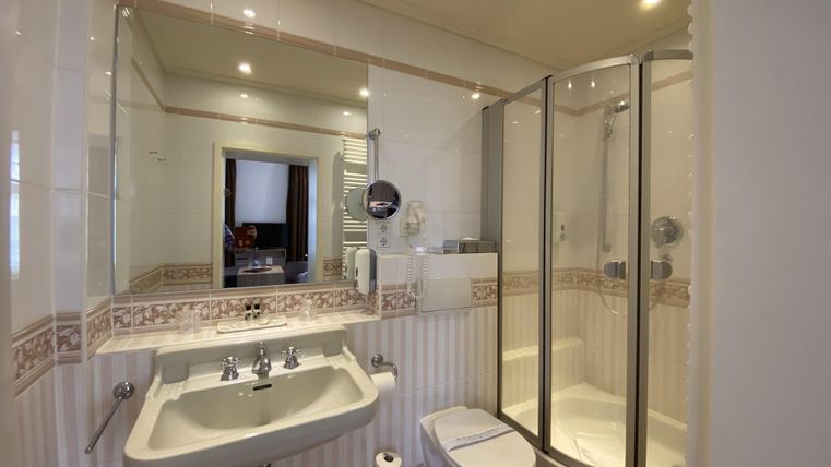 A modern bathroom with a shower, a sink, and a toilet. The walls are bright tiled and well lit.