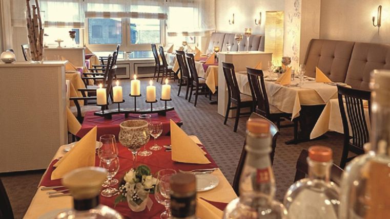 An elegant restaurant with a cozy atmosphere. Tables are decorated with red and yellow tablecloths as well as candles.