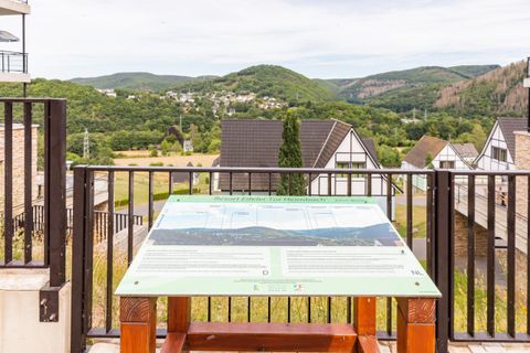 A viewing platform with an information sign that describes the surroundings. In the background, green hills and typical German houses can be seen.