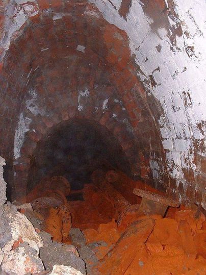 Ein dunkler Tunnel mit verfärbten Wänden und losen Steinen am Boden. Die Umgebung wirkt geheimnisvoll und unheimlich.