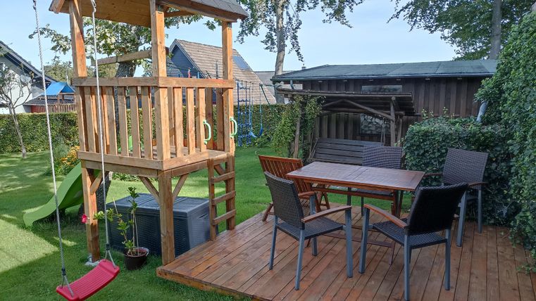 Ein schöner Garten mit einem Spielturm und einer Holzterrasse. Es gibt einen Essbereich mit Stühlen und einem Tisch.