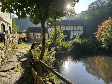 Een schilderachtige vijver omgeven door weelderig groen en bomen. Op de achtergrond is een traditioneel huis in vakwerkstijl te zien.