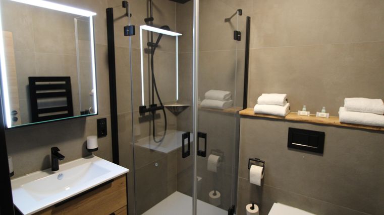 A modern bathroom with a glass shower and elegant fixtures. A towel is ready on the sink, and the space is decorated in neutral colors.
