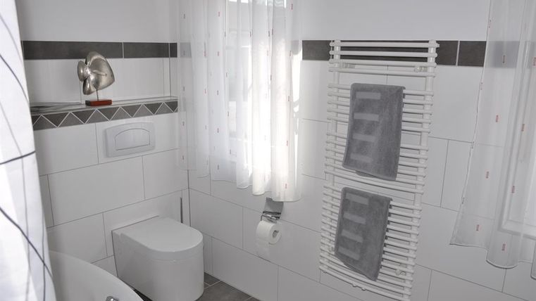 Ein modernes Badezimmer mit weißen Fliesen und einem großen Fenster. Es gibt eine Dusche, Handtücher und eine Fußbodenheizung.