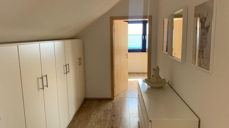 A bright hallway with white cupboards and a modern sideboard. The door leads to another room with a window.