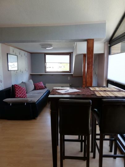 Ein modernes Wohnzimmer mit einem Sofa und einem Tisch. Große Fenster sorgen für viel Licht und eine einladende Atmosphäre.