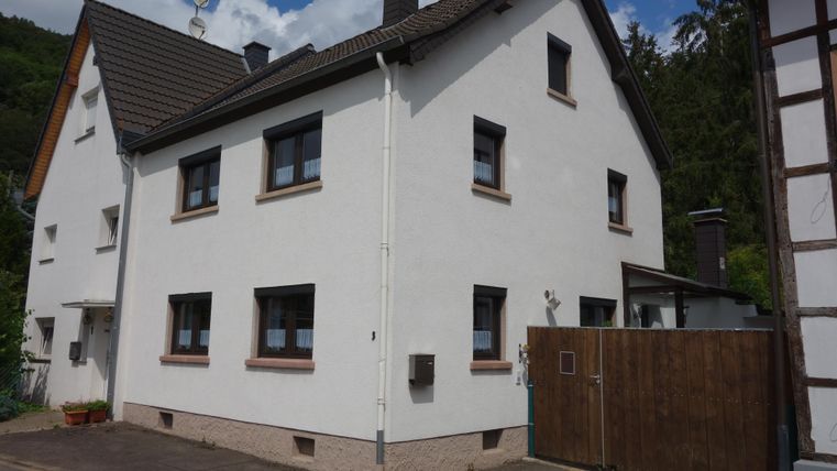 Een modern, tweeledig woonhuis met een witte gevel en een zwart dak. Het bevindt zich in een rustige omgeving met bomen op de achtergrond.