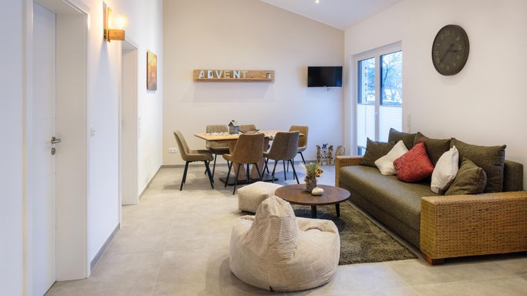Een moderne woonkamer met een comfortabele bank en een grote eettafel. Grote ramen zorgen voor veel natuurlijk licht.
