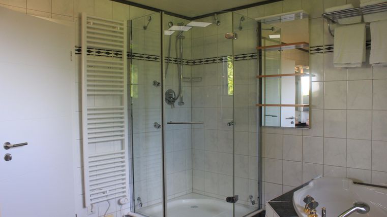 A modern bathroom with a shower and a bathtub. The walls are designed with light tiles and there is a mirror as well as storage space.
