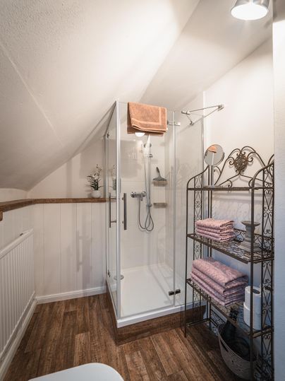 Een moderne badkamer met een douche van glas. Handdoeken zijn netjes op een plank geplaatst.