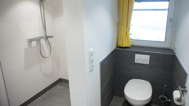 A modern bathroom with a separate shower and a toilet. Bright walls and a window with yellow curtains create a friendly atmosphere.
