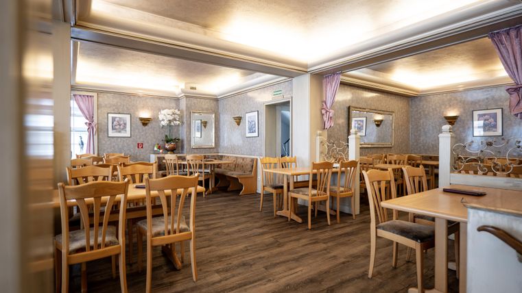 Ein gemütliches Restaurant mit Holztischen und Stühlen. Die Wände sind geschmackvoll dekoriert und die Beleuchtung sorgt für eine einladende Atmosphäre.