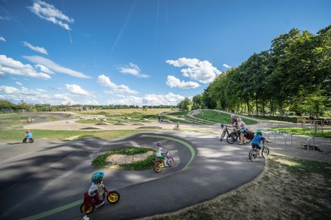 Ein schöner Park mit einer Fahrradstrecke, wo Kinder mit Fahrrädern und Dreirädern fahren. Der Himmel ist klar und die Umgebung ist grün und einladend.