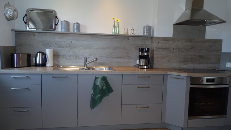 Een moderne keuken met grijze meubels en een houten vloeren. Op het werkblad staan een waterkoker, een koffiezetapparaat en enkele decoratieve elementen.