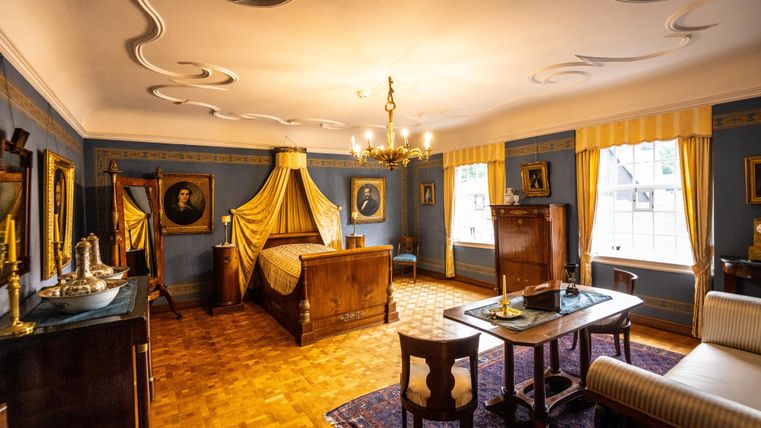 A stylish room with a large bed and elegant decor. The walls are adorned with historic pictures and the light is warm and inviting.