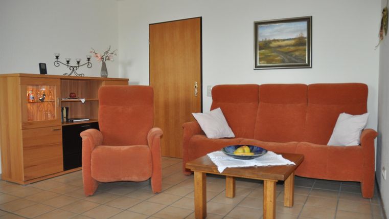 A cozy living room with an orange sofa and a wooden table. The walls are light, and there is a picture as well as a small display cabinet.