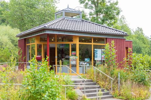 A modern, red-painted building with large windows and a glass roof. Surrounded by green plants and a well-maintained entrance.
