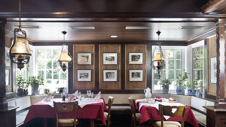 A cozy restaurant with wooden furniture and a warm atmosphere.
Tables are covered with red tablecloths and large windows provide plenty of daylight.
