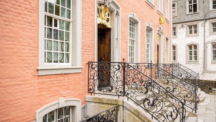 An elegant building with a pink facade and historic windows. The wrought iron railings lead to the front door.