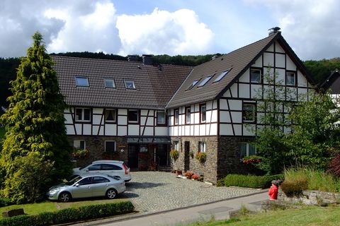 A beautiful half-timbered house with a well-maintained garden. Parked cars are in front of the house, and a person is sitting on the bench.